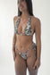 Femme souriante portant un bikini triangle à imprimé animal noir et blanc, photographiée en studio sur fond clair, de profil trois quarts.